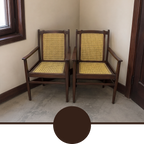 Two wooden armchairs with woven cane seats and backs, shown in a corner room with beige walls and a concrete floor. A large dark brown circular color swatch is overlaid at the bottom of the image.